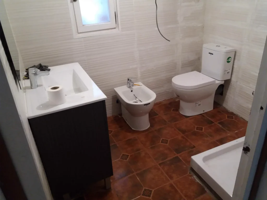 Baño reformado por MZB Gavá con mueble de lavabo, bidé e inodoro nuevos y paredes de azulejo blanco